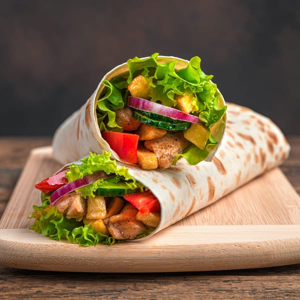 Two Filipino chicken wraps with lettuce, red onion, cucumber, and bell peppers on a wooden board.