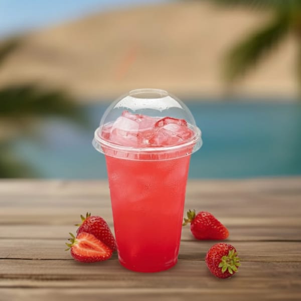 Strawberry drink with ice in a plastic cup, surrounded by fresh strawberries on a wooden table.