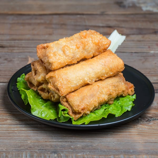 Golden-brown Filipino lumpia spring rolls, stacked on a black plate with fresh green lettuce.